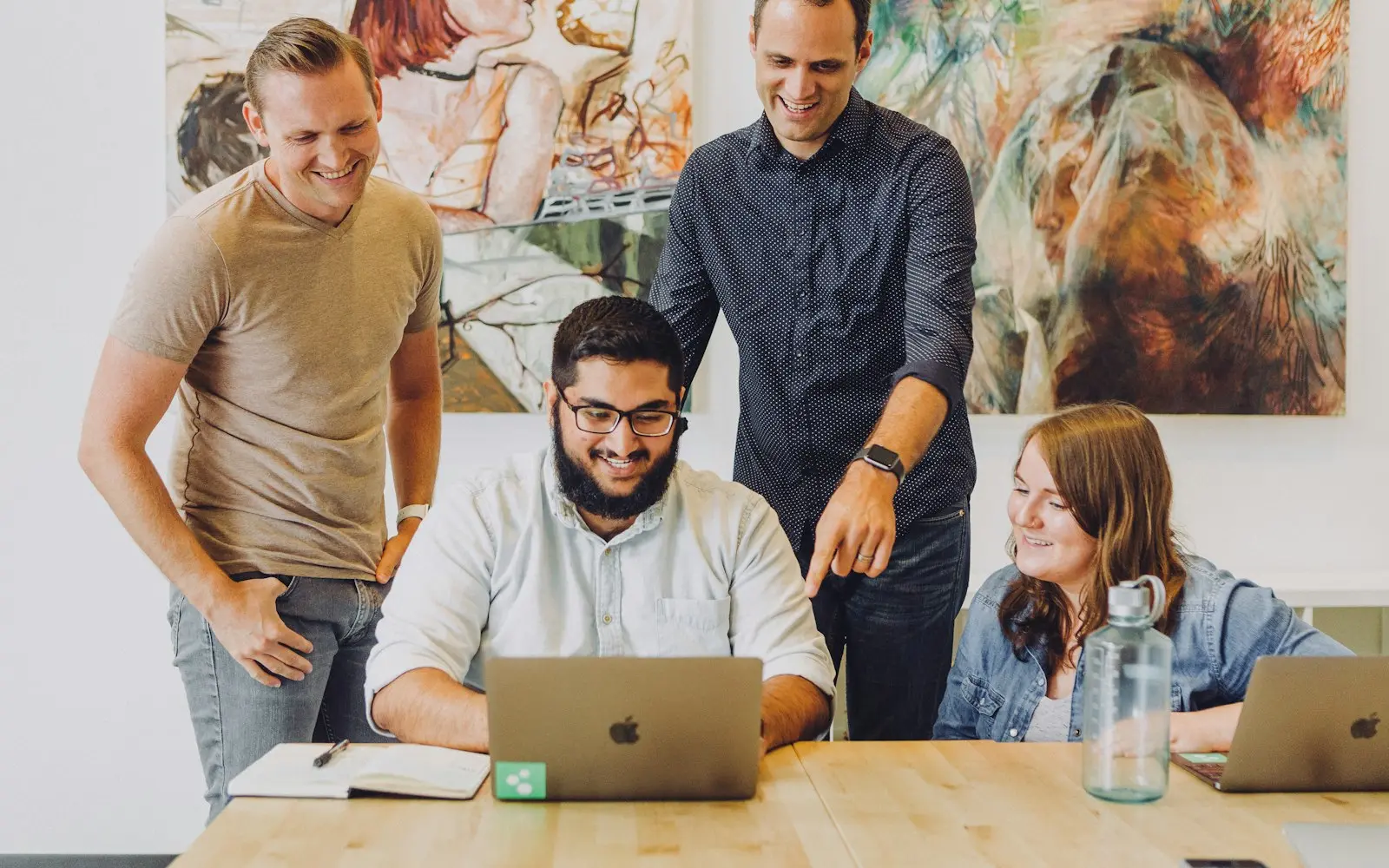 Four colleagues gathered around a laptop at a wooden table in a creative studio