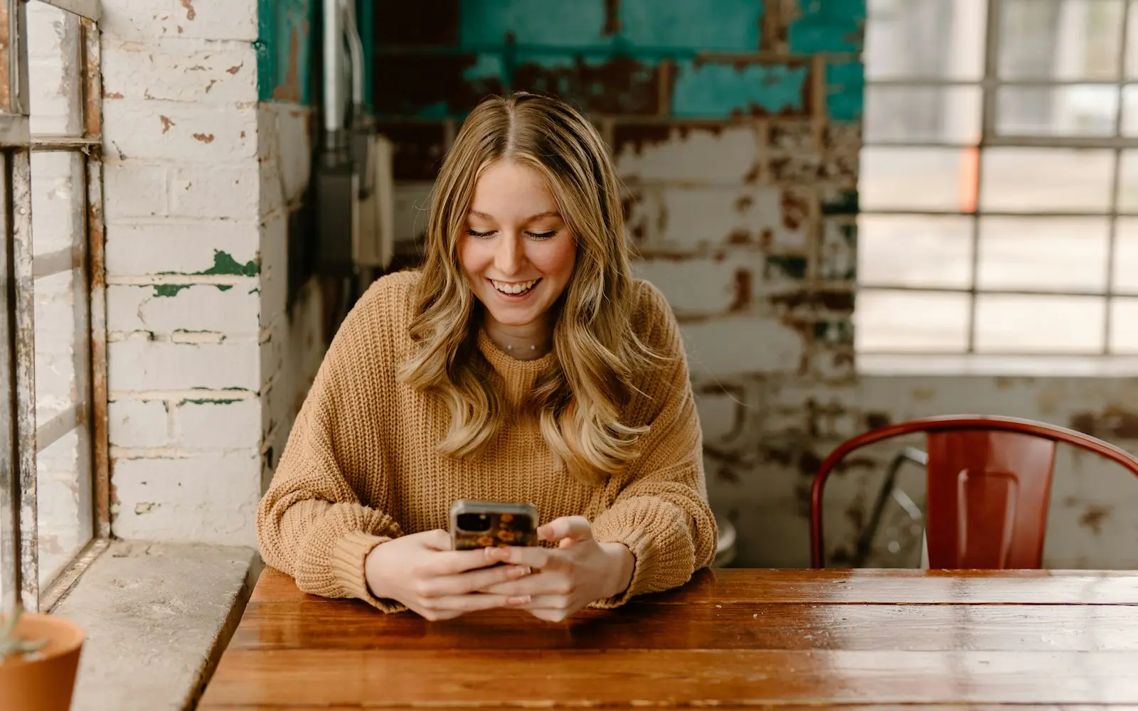 Smiling woman at a wooden table looking at her phone