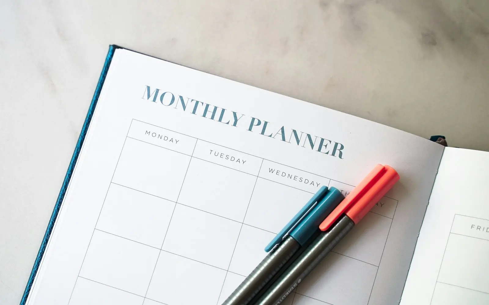 Open monthly planner with two pens on a white desk