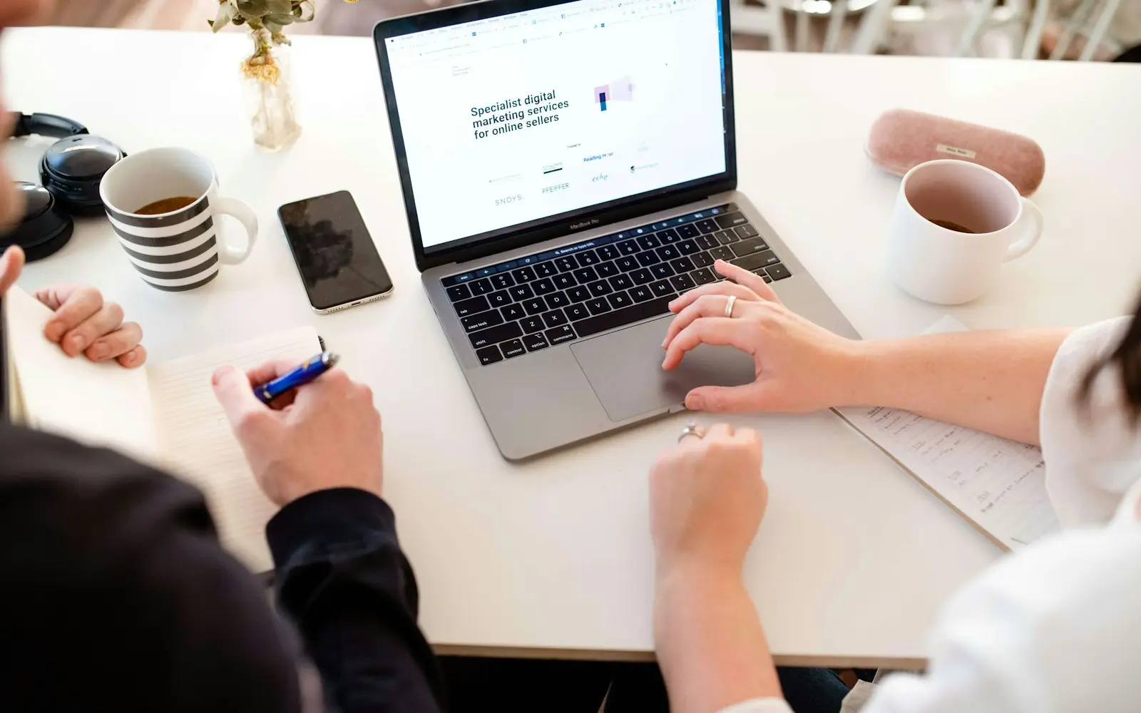 Hands on a laptop and notebook at a table while planning a marketing campaign