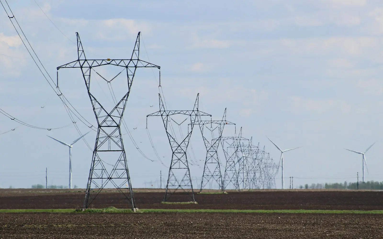 Electricity transmission towers and wind turbines across an open field