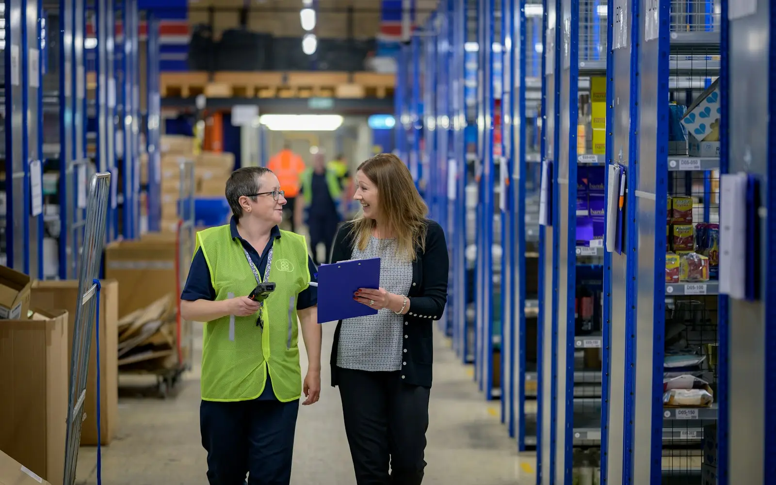 Two warehouse colleagues walking down an aisle of blue shelving