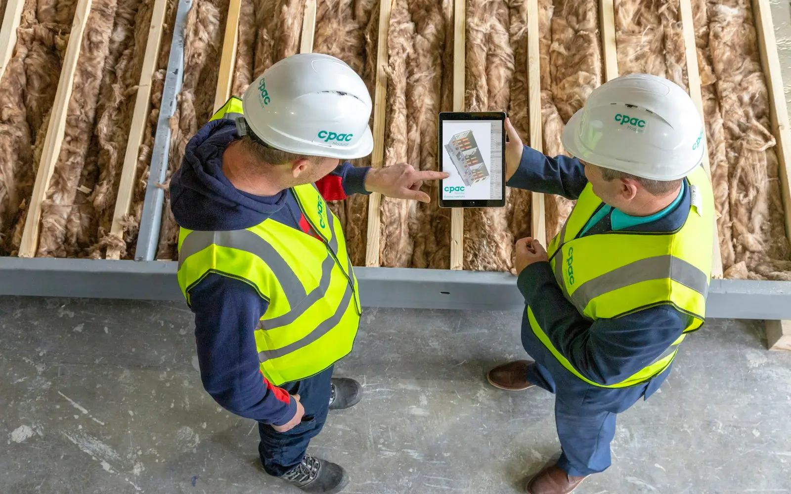 Two site workers in hard hats and hi-vis vests checking a tablet on site