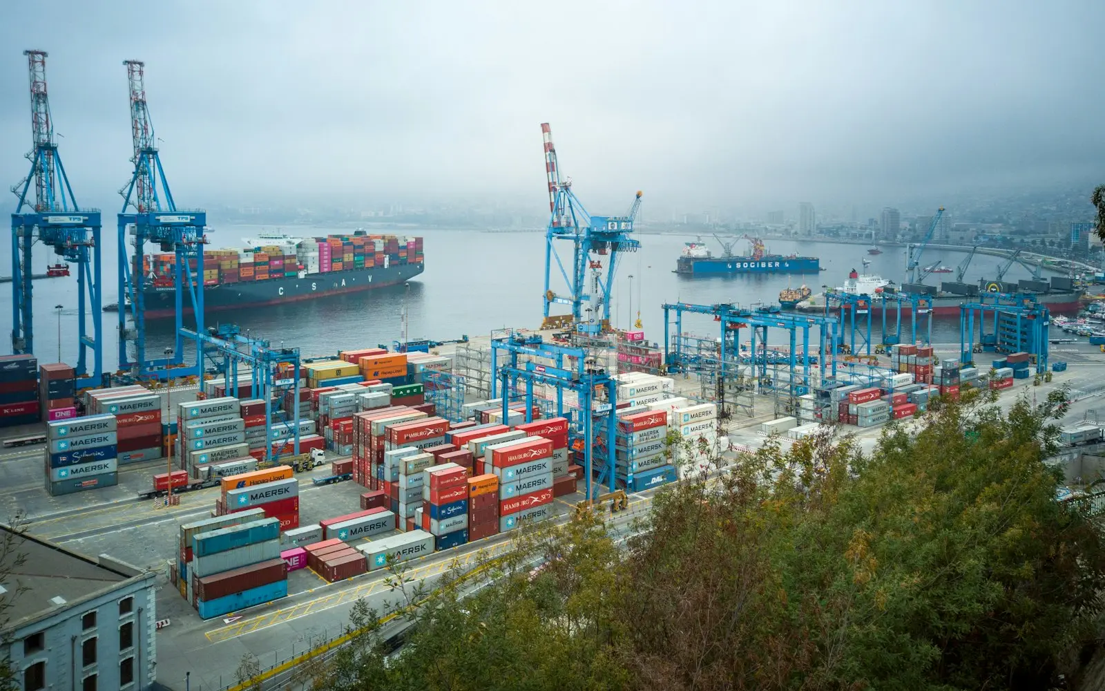 Container port with blue cranes and a cargo ship on misty water