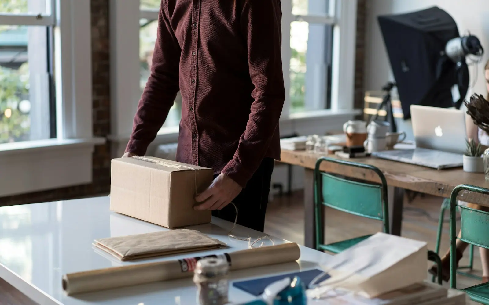 Seller wrapping a cardboard box at a work table in a bright studio