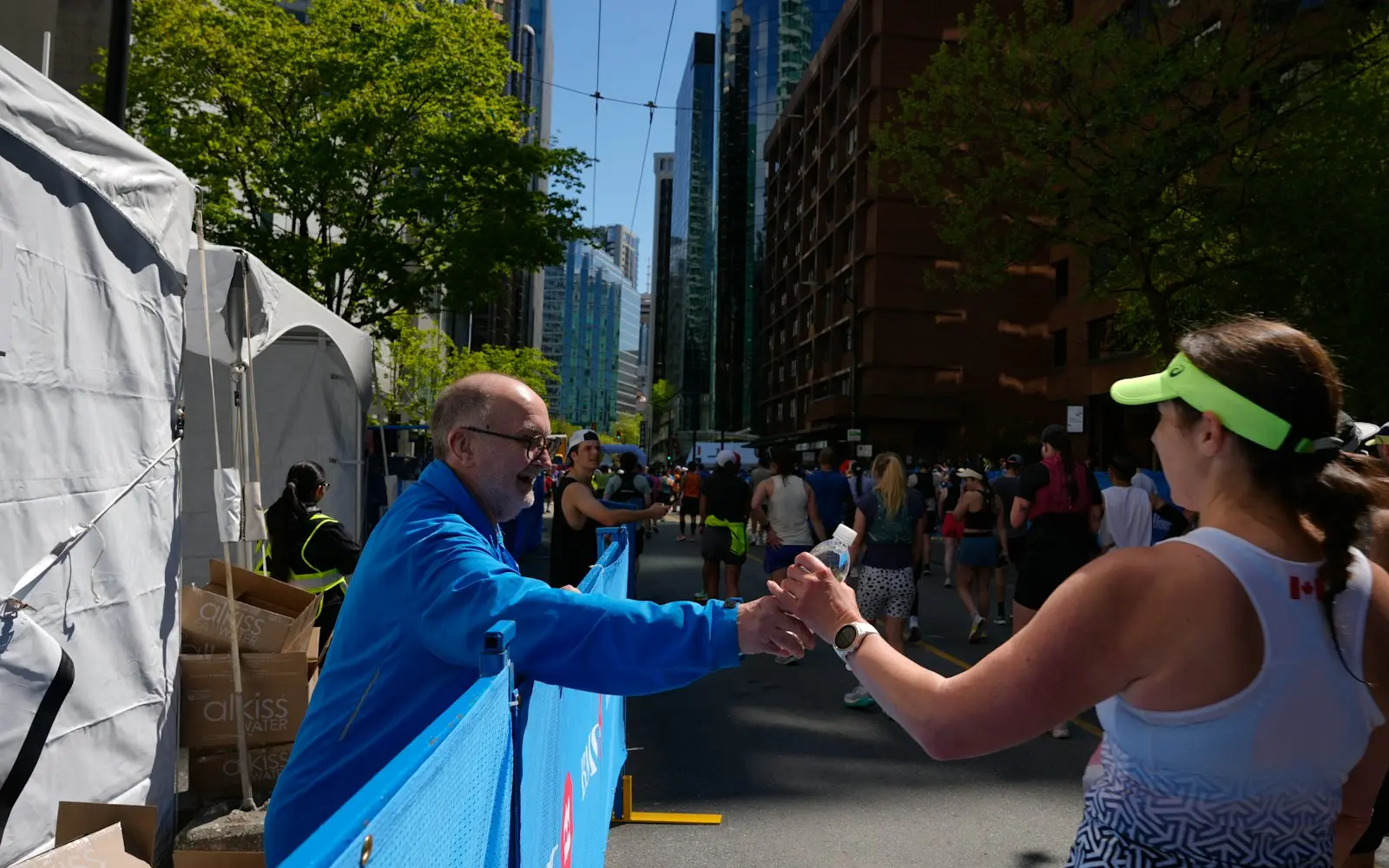Volunteer in a blue jacket handing water to a runner at a city race