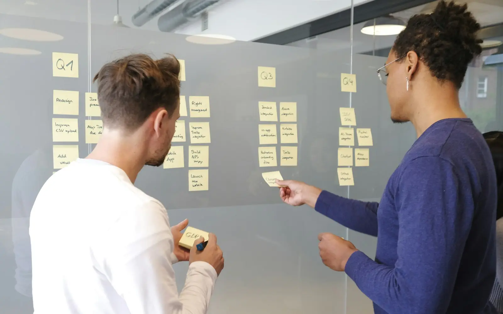 Two colleagues arranging a project plan with sticky notes on a glass wall