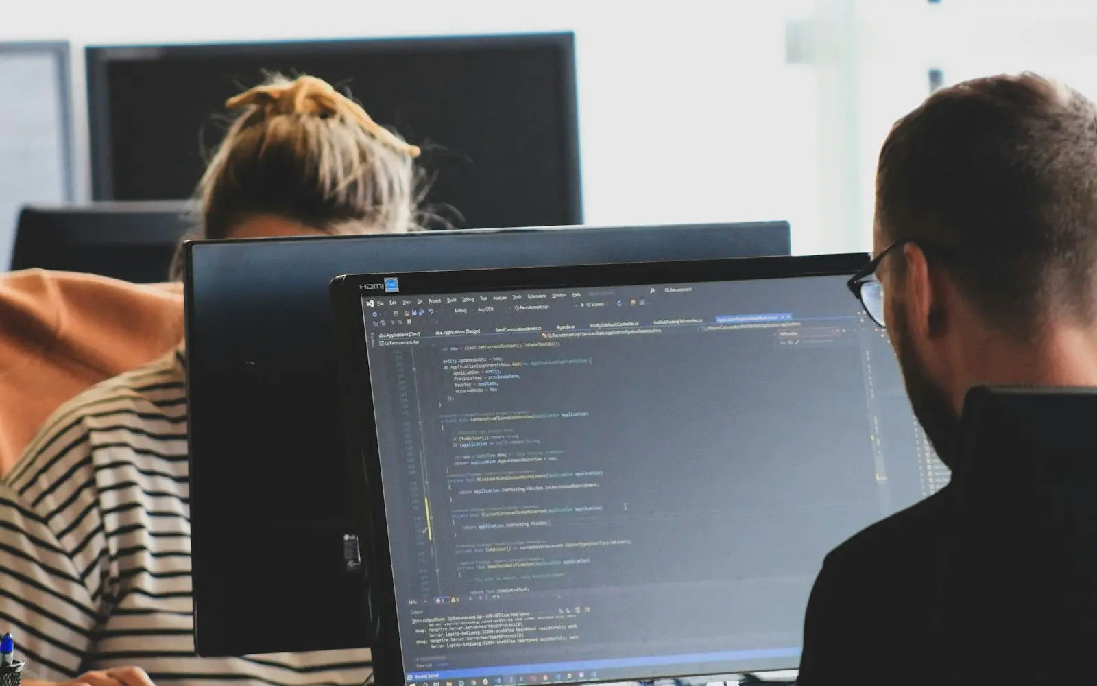 Two developers working on code at monitors in a bright office