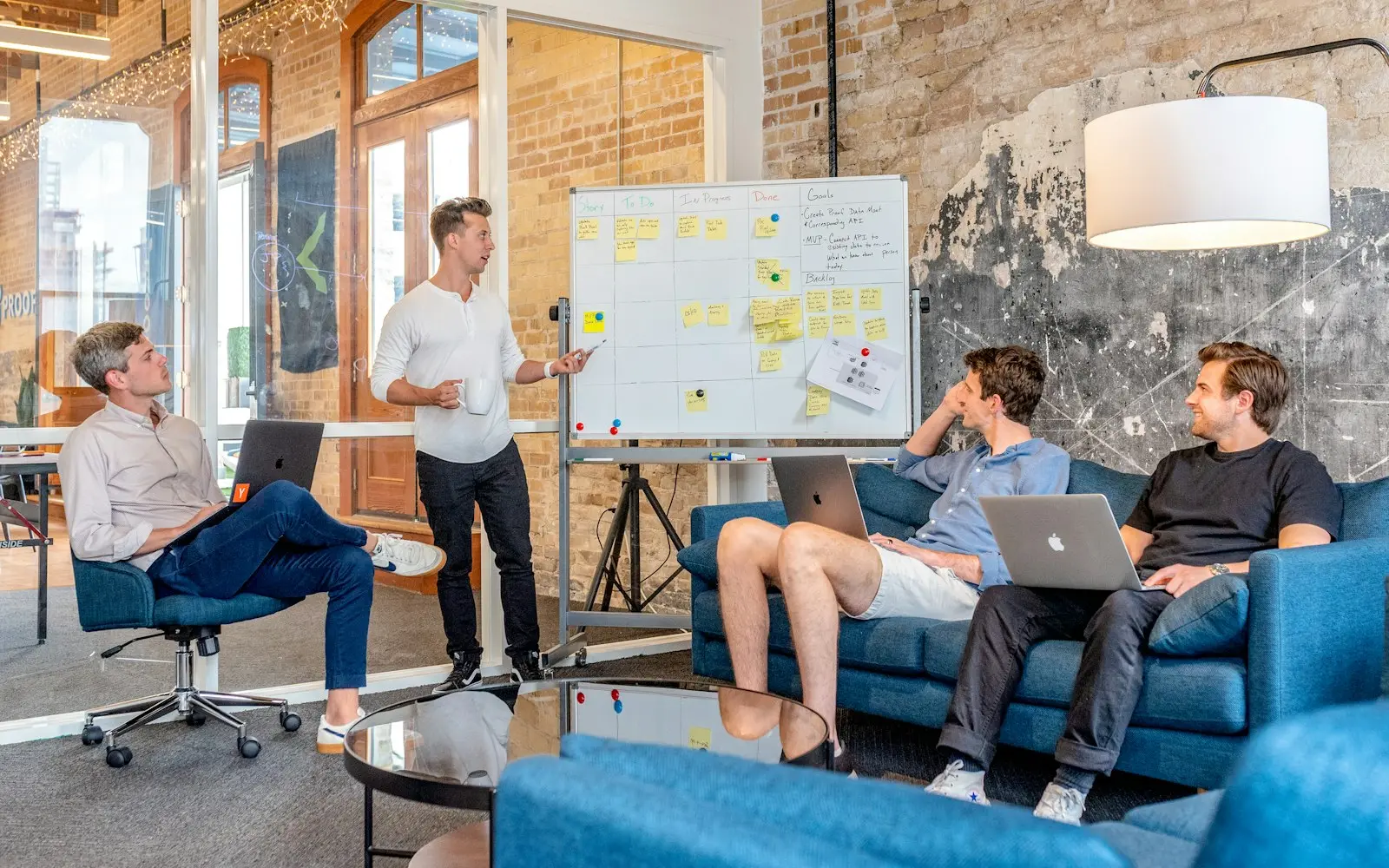 Product team planning at a whiteboard with laptops in a brick-walled loft