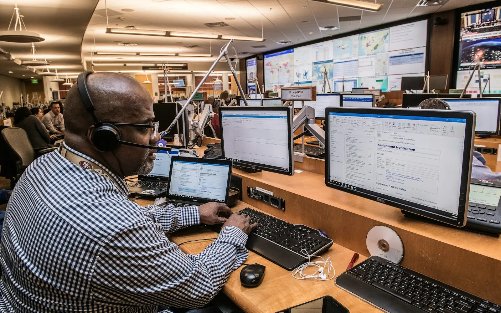 Operator with a headset at a desk of monitors in a large operations centre