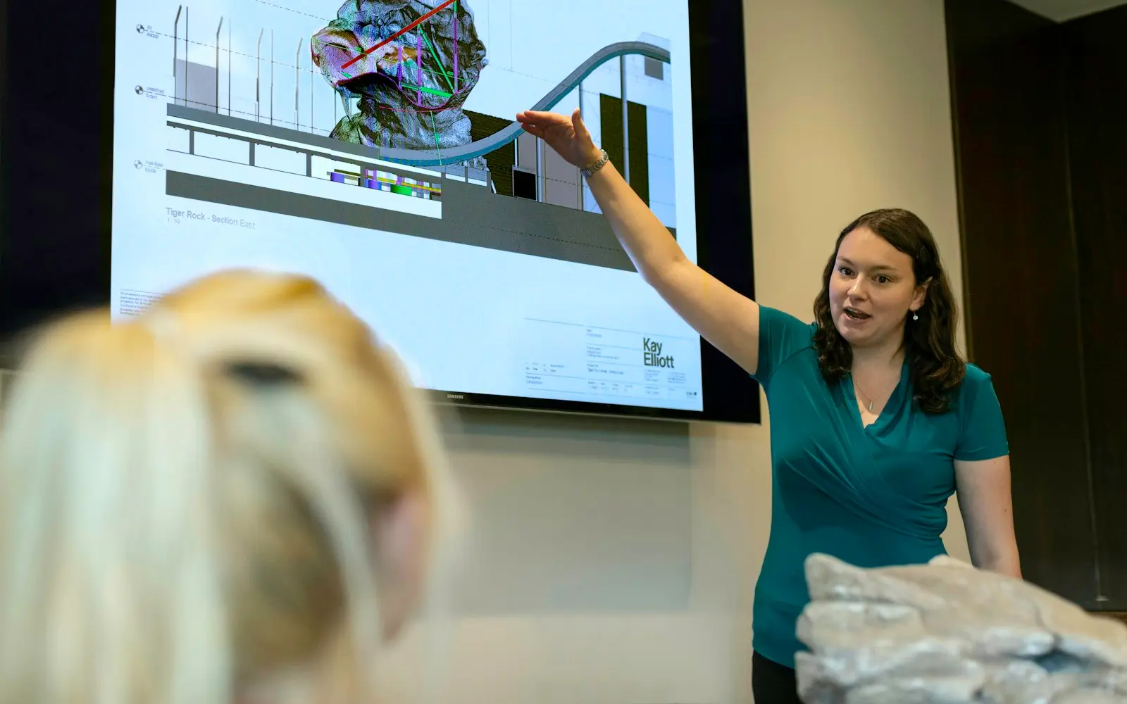 Woman presenting a design on a large wall screen to colleagues