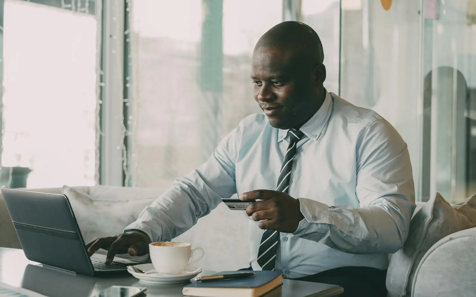 Businessman in shirt and tie using a laptop and bank card at a cafe table