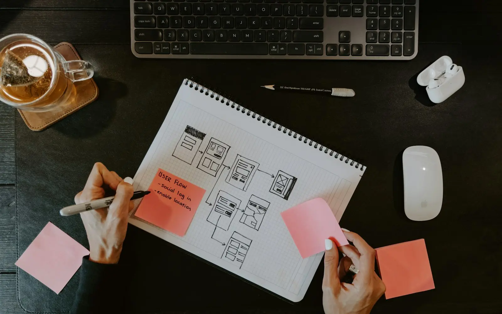 Hands sketching website wireframes in a notebook with sticky notes beside a keyboard
